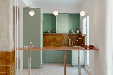 Minimalist kitchen with green cabinets, warm-toned tiles, and modern pendant lights.