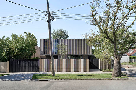 Modern residential building with vertical slatted façade, surrounded by mature trees.