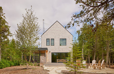 A modern, gabled-roof house nestled in a forested setting with an inviting outdoor patio.