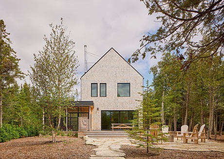 A modern, gabled-roof house nestled in a forested setting with an inviting outdoor patio.