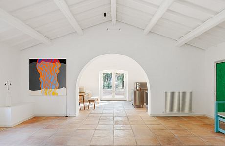 Spacious room with arched windows, wooden beams, and vibrant abstract artwork on walls.