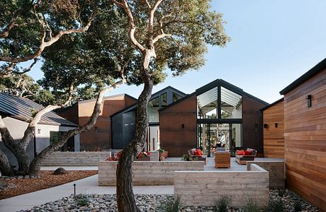 A modern, wooden-paneled home with a large tree and a paved outdoor patio area.