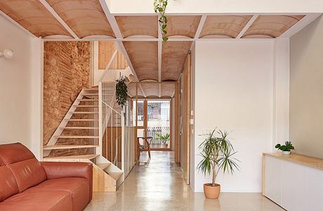 Modern, warm-toned interior with wooden beams, stairs, and potted plants creating a cozy atmosphere.