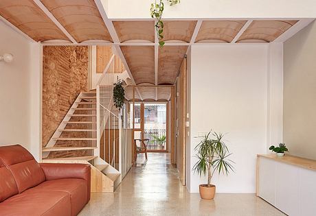 Modern, warm-toned interior with wooden beams, stairs, and potted plants creating a cozy atmosphere.