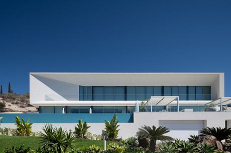 Sleek, modern architecture with expansive glass walls, minimal landscaping, and a pool.