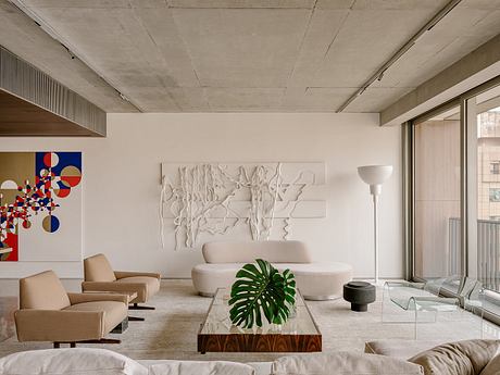 Spacious living room with concrete ceiling, neutral furniture, sculptural wall art, and potted plant.