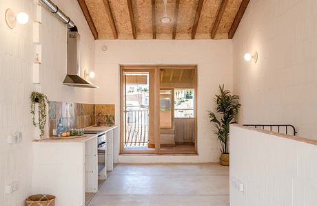 An airy, open-concept kitchen with rustic exposed wood beams and a sliding glass door leading to an outdoor space.