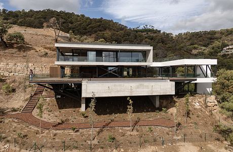 Modern hillside home with expansive glass walls, concrete structure, and raised open-plan design.