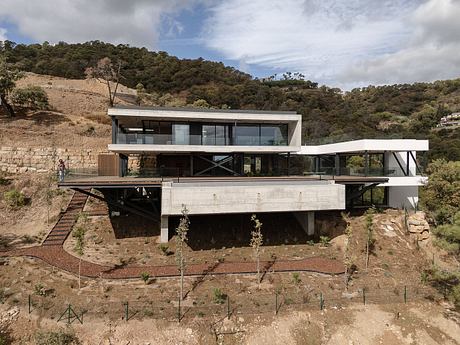 Modern hillside home with expansive glass walls, concrete structure, and raised open-plan design.