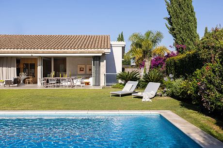 Stucco villa with red-tiled roof, outdoor seating, pool, and lush tropical foliage.