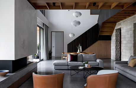 Modern, open-plan living space with wooden ceiling beams, stone walls, and minimalist furniture.