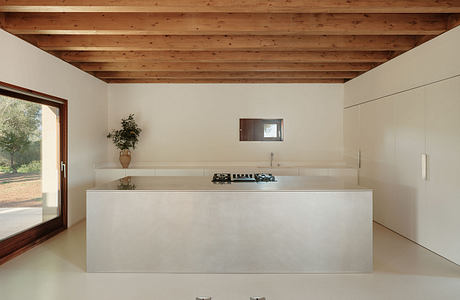 Spacious kitchen with exposed wooden beams, modern concrete counter, and large windows.