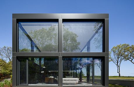 A modern glass-and-steel structure with a spacious outdoor seating area surrounded by lush greenery.