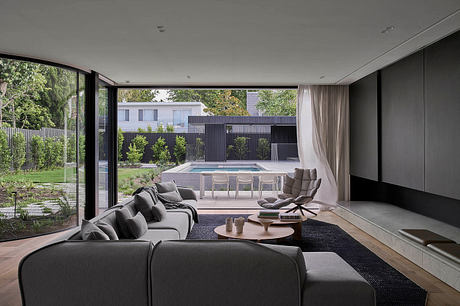 Modern living room with glass walls, minimalist furnishings, and outdoor seating area.