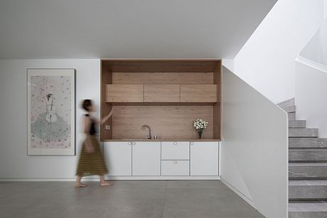 The image showcases a minimalist kitchen design with wooden panels, white cabinets, and a staircase leading upstairs.