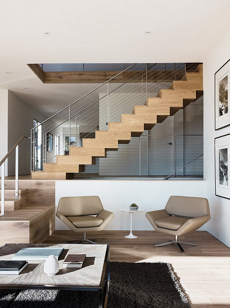 Sleek and modern staircase with wooden steps and metal railing, accented by neutral-toned furniture.