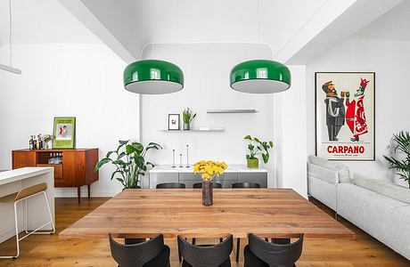 Bright, minimalist dining space with wooden table, hanging green lamps, and framed artwork.