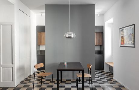 A modern dining room with a checkered tile floor, a black table, and wooden chairs. A sleek pendant light fixture hangs above the table.