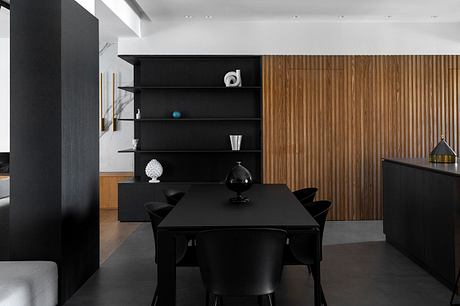 Modern dining room with black furniture, wooden paneling, and minimalist decor.