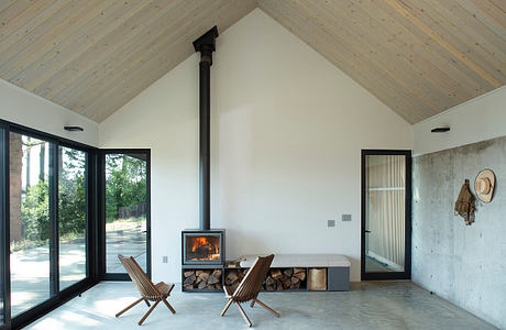 A cozy cabin interior with large windows, rustic wood ceiling, and a central fireplace.