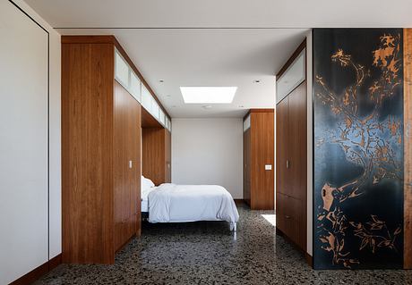 Spacious modern bedroom with wood cabinetry, ornate wall panel, and skylight.