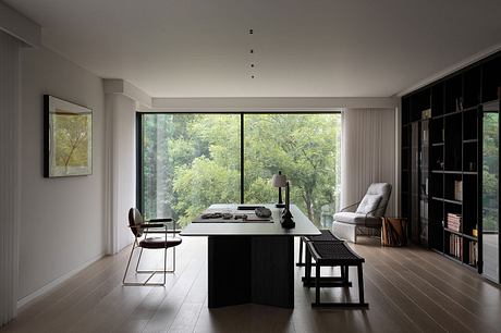 Minimalist home office with large windows, dark furniture, and nature-inspired artwork.
