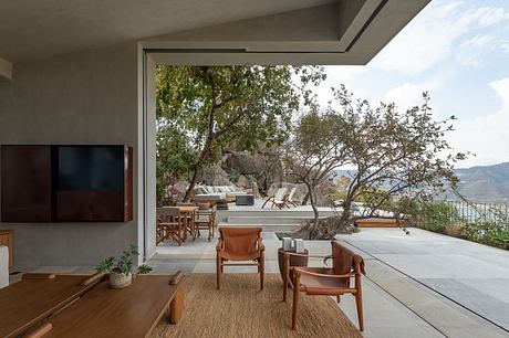 Expansive glass walls frame a lush, natural landscape with sleek, modern furnishings.