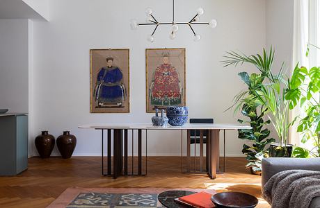 Elegant modern dining room with ornate Chinese artwork, lush plants, and minimalist furniture.