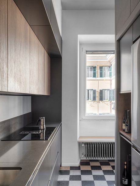 Sleek kitchen design with black countertop and wooden cabinetry, leading to a hallway with a checkered floor.