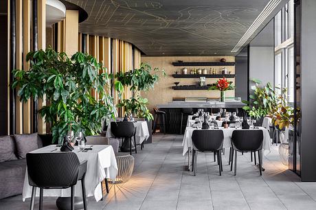 Stylish restaurant interior with modern furniture, leafy plants, and intricate ceiling design.