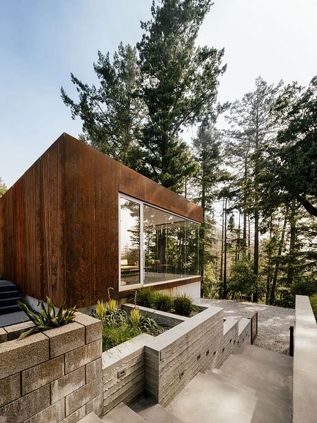 A modern, wooden cabin with floor-to-ceiling windows nestled in a lush, forested setting.