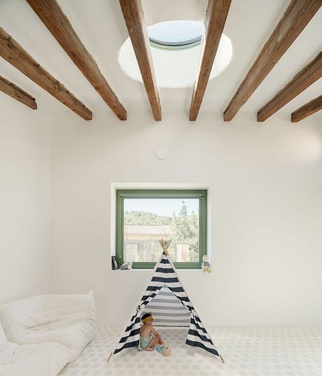 Cozy, airy space with wooden beams, a large window, and a striped tent for a child.