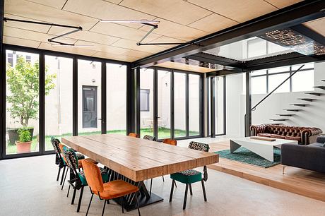 Spacious open-concept interior with a large wooden dining table, plush seating, and floor-to-ceiling windows overlooking a lush outdoor space.