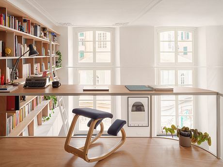 Minimalist office space with bookshelves, large windows, and a rocking chair desk setup.