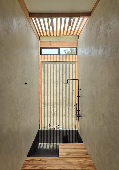 Rustic shower stall with wooden slat ceiling, concrete walls, and black metal fixtures.