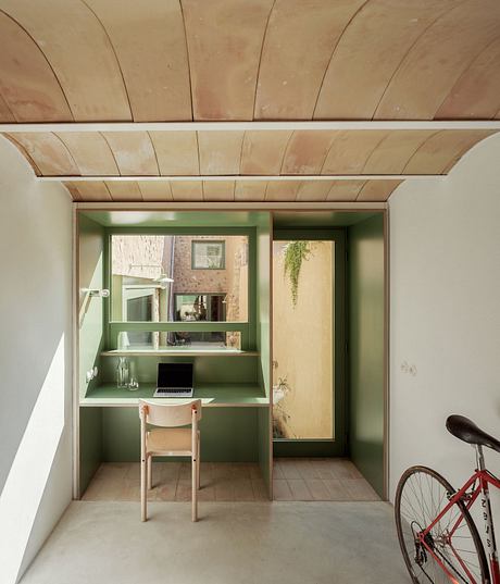 A cozy workspace nook with built-in shelving, wooden ceiling, and a red bicycle.