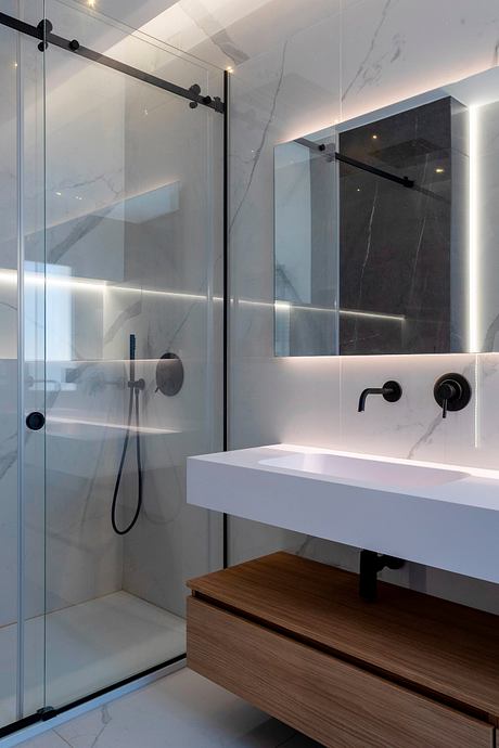 Sleek and modern bathroom with glass shower, marble walls, and a wooden vanity.