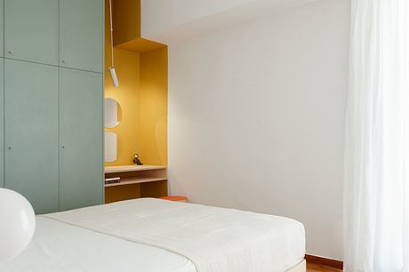 Minimalist bedroom with built-in green cabinets, warm orange accents, and a simple bed.
