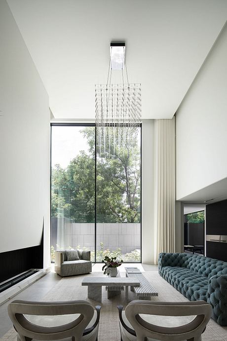 Minimalist living room with modern chandelier, large sofa, and expansive windows overlooking nature.