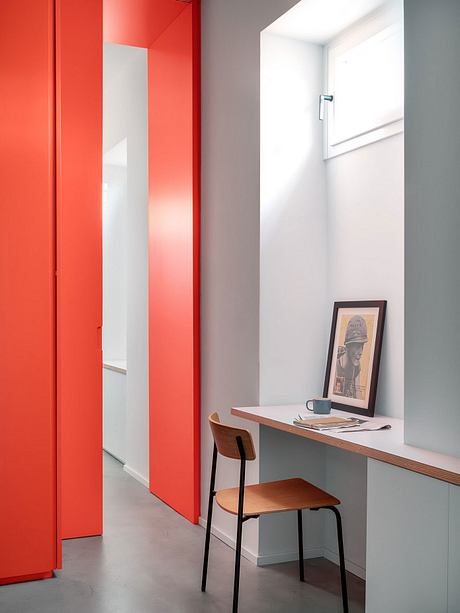 Vibrant red closet doors contrast with muted gray walls, creating a modern look. Sleek desk and chair complete the minimalist design.