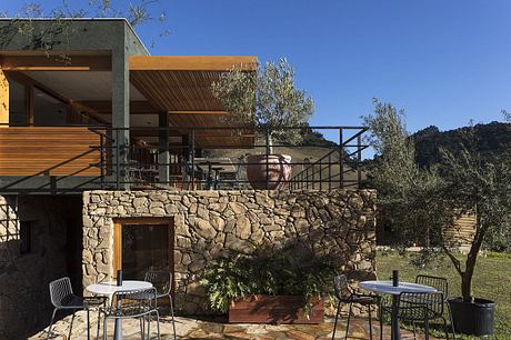 Rustic stone exterior with wooden beams, outdoor seating area overlooking lush landscape.