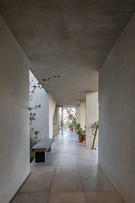 A minimalist, concrete hallway with a long stone bench, lush plants, and natural lighting.