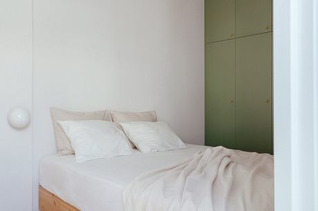 Minimalist bedroom with neutral-toned bedding, built-in green cabinetry, and spherical wall light.