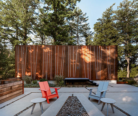 Striking contemporary outdoor space with bold red and blue chairs, metal fire pit, and wooden wall.