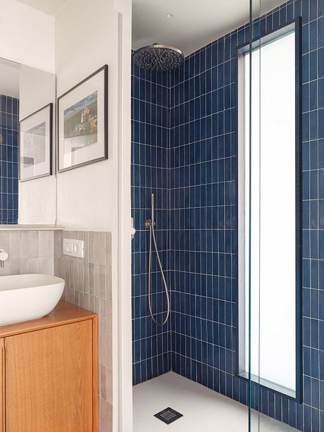 Modern bathroom with navy blue tiled walls, wooden vanity, and glass shower enclosure.