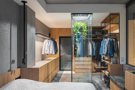 Sleek, minimalist bedroom with glass wall closet, wooden accents, and indoor plants.