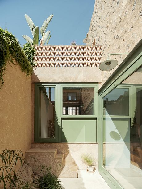 A cozy courtyard with geometric lattices, lush plants, and a glass-enclosed entryway.