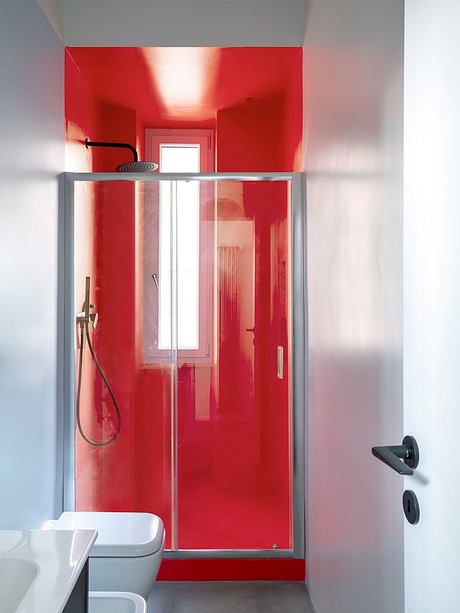 Vibrant red bathroom with sliding glass shower door and minimalist fixtures.