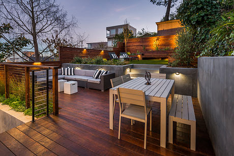 Elegant outdoor deck with modern wooden furniture, lighting, and landscaping elements.
