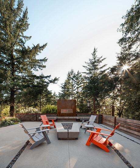 Outdoor seating area with modern Adirondack chairs around a concrete fire pit, surrounded by trees.